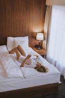 mujer feliz usando un teléfono móvil mientras está acostado en la cama foto