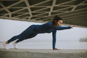 Young woman in blue track suit doing pushups in the urban environment photo