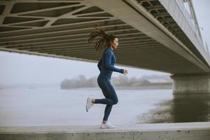 Young woman in blue track suit running by the river at autumn morning photo