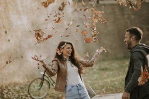 Pareja joven divirtiéndose con hojas de otoño en el parque foto