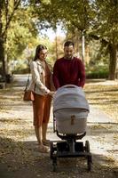 Happy young parents walking in the park and driving a baby in baby carriage photo