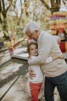 Grandfather having fun with his little granddaughter in the amusement park photo