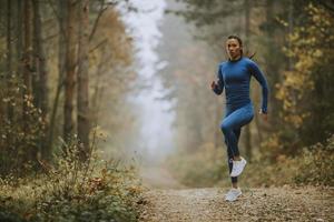 Mujer joven corriendo haciendo ejercicio en la pista forestal en otoño foto