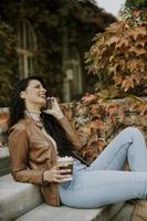 Mujer joven con teléfono móvil beber café para ir a las escaleras exteriores el día de otoño
