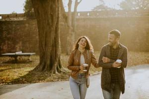 Young couple walking in autumn park with takeaway coffee cups in hands photo