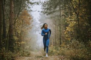 Mujer joven corriendo hacia la cámara en la pista forestal en otoño foto