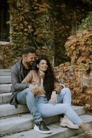 pareja joven sentada en las escaleras al aire libre en un día de otoño y usando un teléfono móvil foto