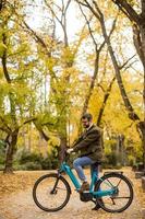 Joven con bicicleta eléctrica en el parque de otoño foto
