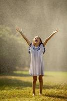 Cute little girl having fun under irrigation sprinkler photo