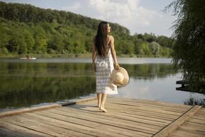 Relaxing young woman standing on wooden pier at the lake photo