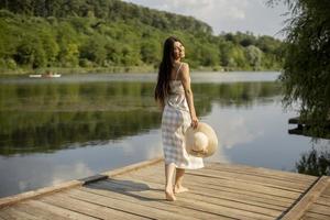 Relaxing young woman standing on wooden pier at the lake photo