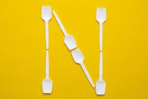 White plastic spoons in the form of letter N on yellow background. Top view. Copy, empty space for text photo
