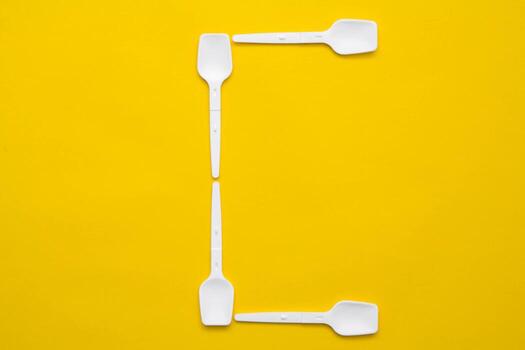 White plastic spoons in the form of letter C on yellow background. Top view. Copy, empty space for text photo