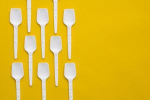 White plastic spoons on yellow background. Fast food, eco and no plastic concept. Top view. Copy, empty space for text photo