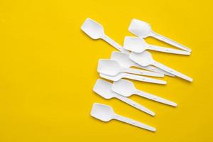 White plastic spoons on yellow background. Fast food, eco and no plastic concept. Top view. Copy, empty space for text photo