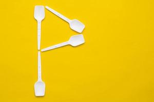 White plastic spoons in the form of letter P on yellow background. Top view. Copy, empty space for text photo