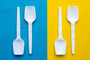 White plastic spoons on blue and yellow background. Fast food, eco and no plastic concept. Top view. Copy, empty space for text photo