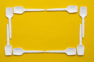 White plastic spoons on yellow background. Fast food, eco and no plastic concept. Top view. Copy, empty space for text photo