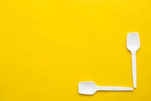 White plastic spoons on yellow background. Fast food, eco and no plastic concept. Top view. Copy, empty space for text photo