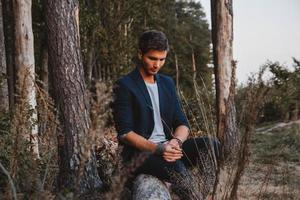 guapo posando al aire libre en el bosque se sienta en un tronco, vistiendo chaqueta a cuadros. lugar para texto o publicidad foto