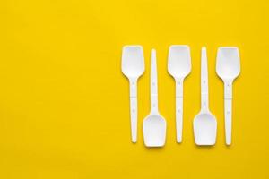 White plastic spoons on yellow background. Fast food, eco and no plastic concept. Top view. Copy, empty space for text photo