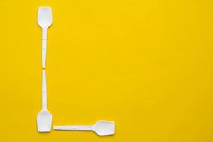 White plastic spoons in the form of letter L on yellow background. Top view. Copy, empty space for text photo