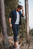 Handsome man posing outdoors in forest stands barefoot on a log, wearing checked jacket. Place for text or advertising photo
