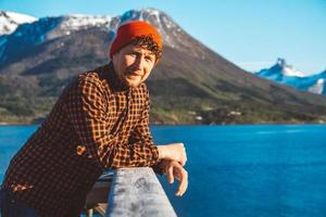 Portrait of young man standing on a wooden pier on background of mountains and lake. Place for text or advertising photo