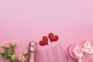 Top view two red hearts, glasses, champagne, flowers on a pink background with copy space valentines day date or party concept photo