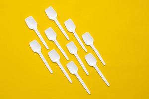 White plastic spoons on yellow background. Fast food, eco and no plastic concept. Top view. Copy, empty space for text photo