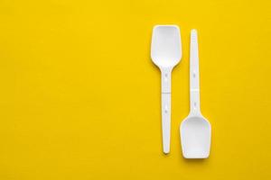 White plastic spoons on yellow background. Fast food, eco and no plastic concept. Top view. Copy, empty space for text photo