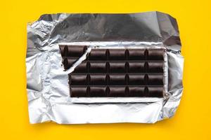 Barra de chocolate en lámina de plata sobre fondo amarillo foto
