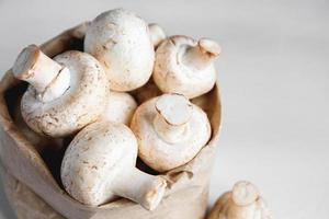 Mushrooms champignons in paper bag on a white wooden table. Close up. Place for text or advertising photo