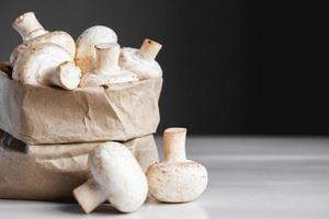 Mushrooms champignons in paper bag on a white wooden table. Place for text or advertising photo