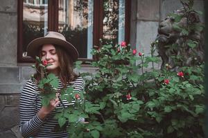 Retrato de joven bella mujer con sombrero cerca de flores rosas foto