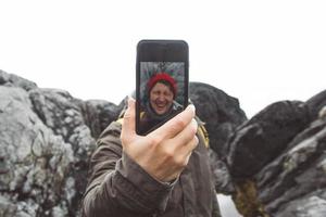 Traveler man taking self-portrait with a smartphone against the background of mountains and rocks. Place for text or advertising photo