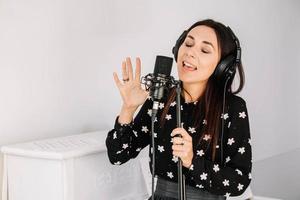 Beautiful woman in headphones sings a song near a microphone in a recording studio. Place for text or advertising