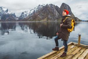 joven con una mochila de pie sobre un muelle de madera el fondo de montañas nevadas y el lago. lugar para texto o publicidad foto