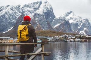 joven con una mochila de pie sobre un muelle de madera el fondo de montañas nevadas y el lago. lugar para texto o publicidad