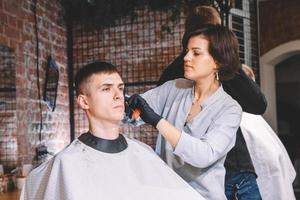 Peluquería de mujer hermosa hace un corte de pelo en la cabeza del cliente con una recortadora eléctrica en peluquería. concepto de publicidad y peluquería. lugar para texto o publicidad
