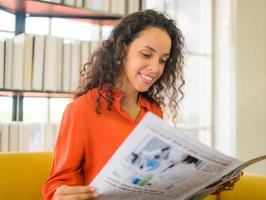 Mujer de América Latina leyendo el periódico en el sofá foto