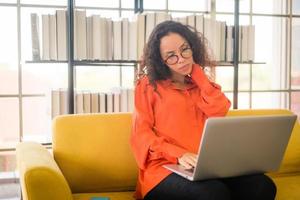 Latin woman working with laptop on sofa with tired feeling
