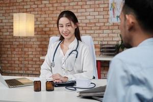 Beautiful woman doctor in white shirt who is Asian person with stethoscope is health examining male patient in brick wall background medical clinic, smiling advising medical specialist occupation. photo