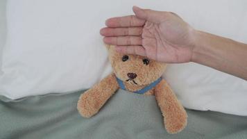 nausées et fièvre. en utilisant un ours comme représentation d'enfant. les hommes mesurent la température de la tête avec leurs mains et utilisent un gel rafraîchissant pour réduire la fièvre.