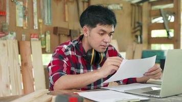 Kleinunternehmer Zimmerei Konzept. asiatischer Mann, der ein Holzmöbelgeschäft besitzt, misst das Holz. Der Tischler misst die Länge des Holzes, um die Produktionszeichnungen zu erfüllen.