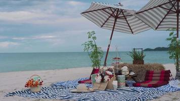 cesta de piquenique com comida na praia. céu limpo e praias de areia branca ao som das ondas e vista mar. conceito relaxar e viajar. video