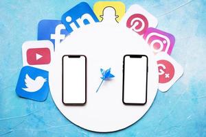 Iconos de aplicaciones móviles sociales alrededor de un marco blanco circular con dos teléfonos móviles contra el fondo azul