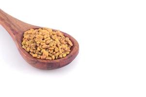 Fenugreek seeds in wooden spoon isolated on white background photo