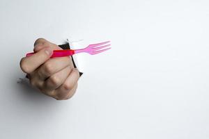 mano femenina sosteniendo un tenedor de plástico rojo sobre un fondo blanco. foto