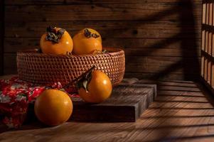 Persimmons on the plate are on the wooden table in dark light photo